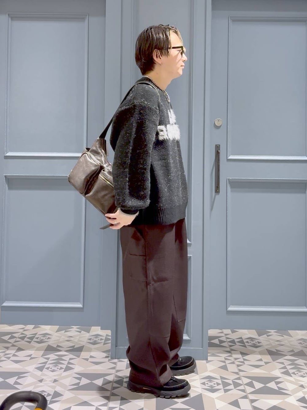 ブラウン系のショルダーバッグ、ブラック系のニット/セーター、ブラウン系のスラックスを着用したメンズの秋コーディネートの2枚目の写真