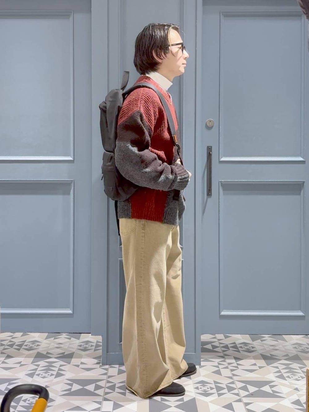 ベージュ系のデニムパンツ、ブラック系のバックパック/リュック、レッド系のニット/セーターを着用したメンズの冬コーディネートの2枚目の写真