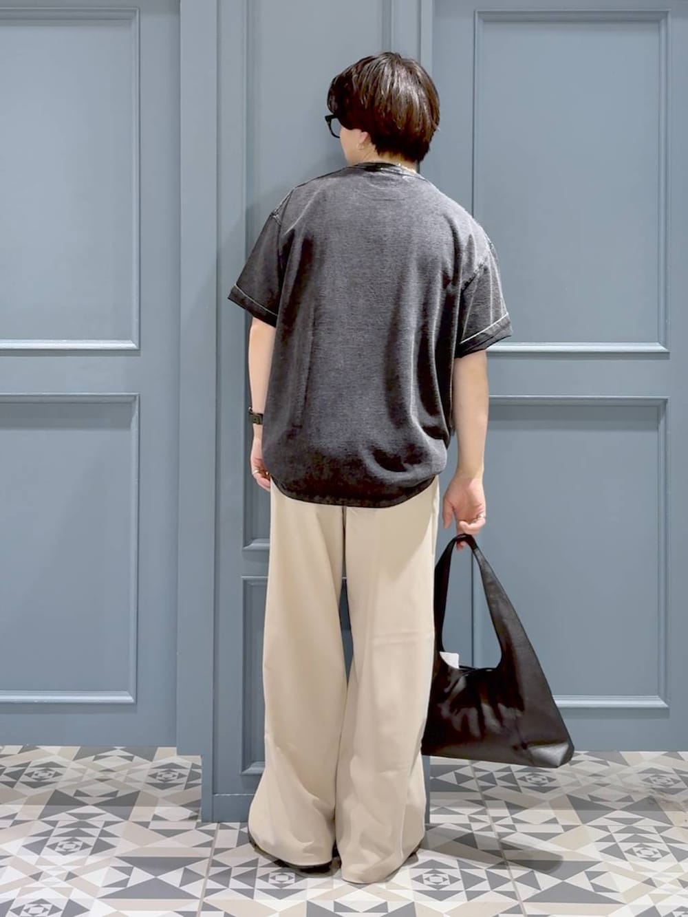 ブラック系のスニーカー、ホワイト系のスラックス、ブラック系のトートバッグを着用したメンズの夏コーディネートの3枚目の写真