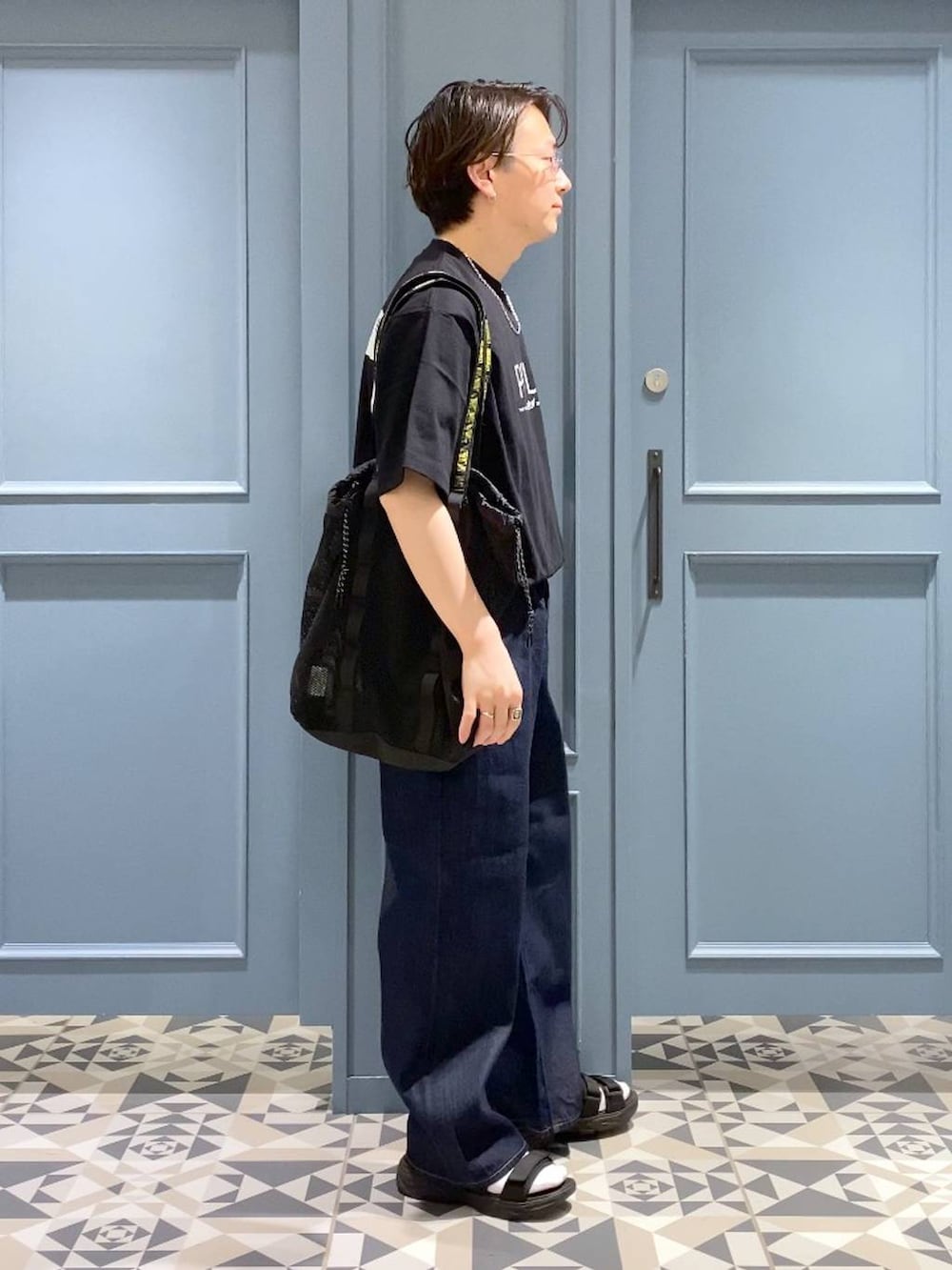 ブルー系のデニムパンツ、ブラック系のサンダル、ブラック系のトートバッグを着用したメンズの春コーディネートの2枚目の写真