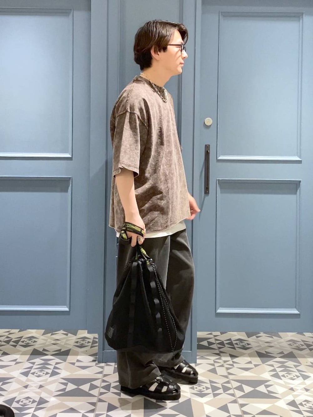 ブラウン系のTシャツ/カットソー、ブラック系のトートバッグ、ブラック系のサンダルを着用したメンズの春コーディネートの2枚目の写真