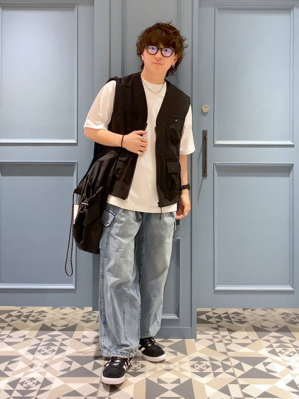 ブルー系のデニムパンツ、ブラック系のショルダーバッグ、ブラック系のベストを着用したメンズの夏コーディネートの4枚目の写真