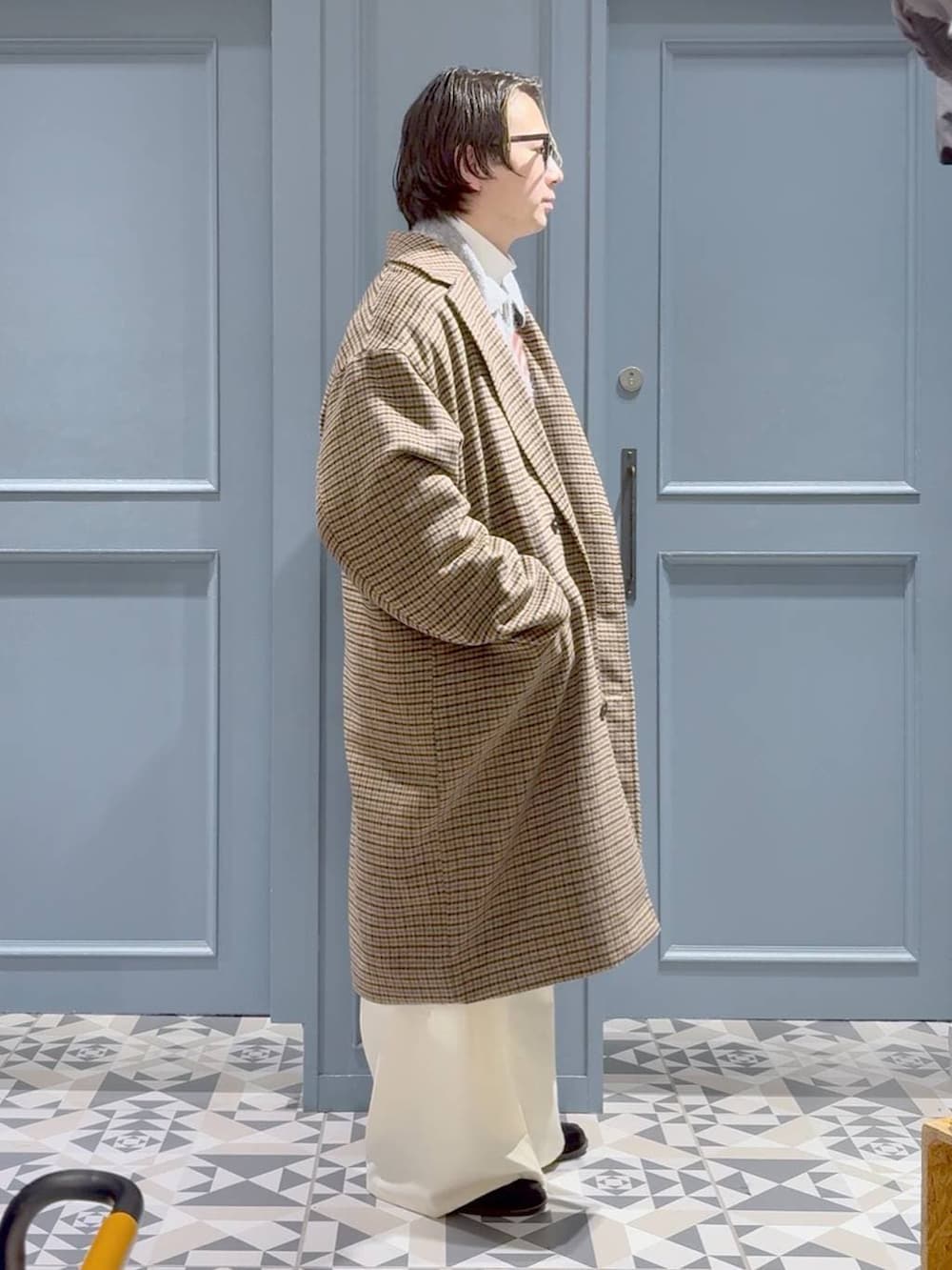 ブラウン系のチェスターコート、グレー系のポロシャツ、ホワイト系のスラックスを着用したメンズの冬コーディネートの2枚目の写真