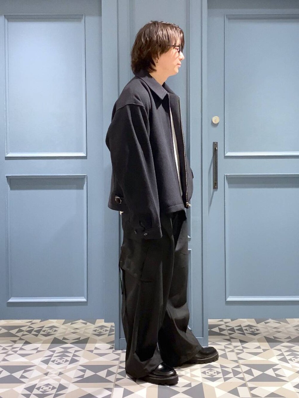 ブラック系のブルゾン、ブラック系のドレスシューズ、ブルー系のニット/セーターを着用したメンズの冬コーディネートの2枚目の写真