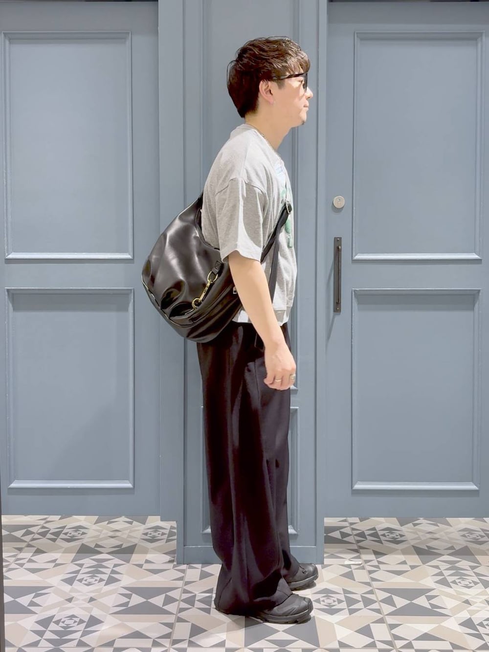 ブラック系のスラックス、ブラック系のスニーカー、ブラック系のショルダーバッグを着用したメンズの春コーディネートの2枚目の写真