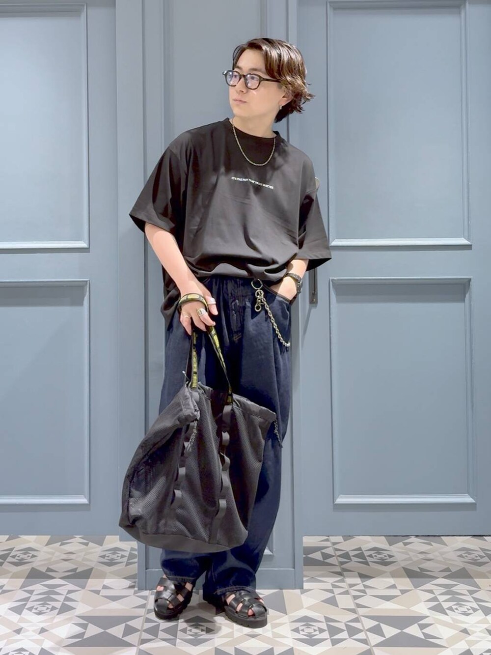 ブラック系のトートバッグ、ブラック系のサンダル、ブルー系のデニムパンツを着用したメンズの夏コーディネートの4枚目の写真