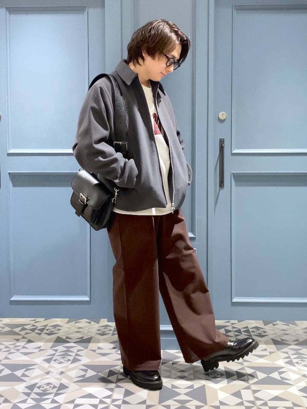 グレー系のブルゾン、ブラウン系のスラックス、ブラック系のショルダーバッグを着用したメンズの冬コーディネートの4枚目の写真