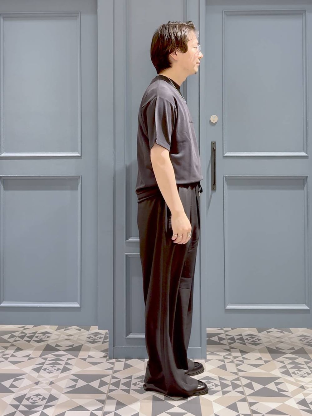 ブラック系のローファー、グレー系のスラックス、ブラック系のTシャツ/カットソーを着用したメンズの夏コーディネートの2枚目の写真