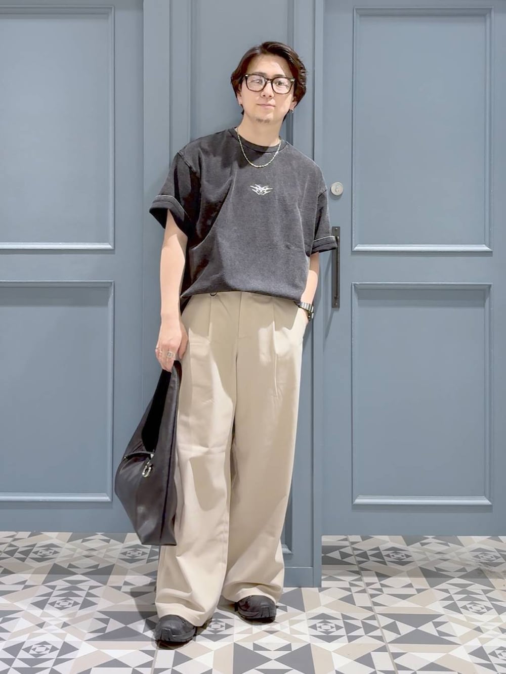 ブラック系のスニーカー、ホワイト系のスラックス、ブラック系のトートバッグを着用したメンズの夏コーディネートの4枚目の写真