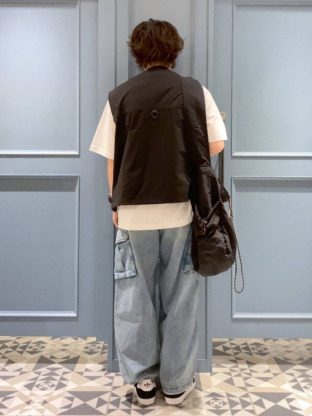 ブルー系のデニムパンツ、ブラック系のショルダーバッグ、ブラック系のベストを着用したメンズの夏コーディネートの3枚目の写真