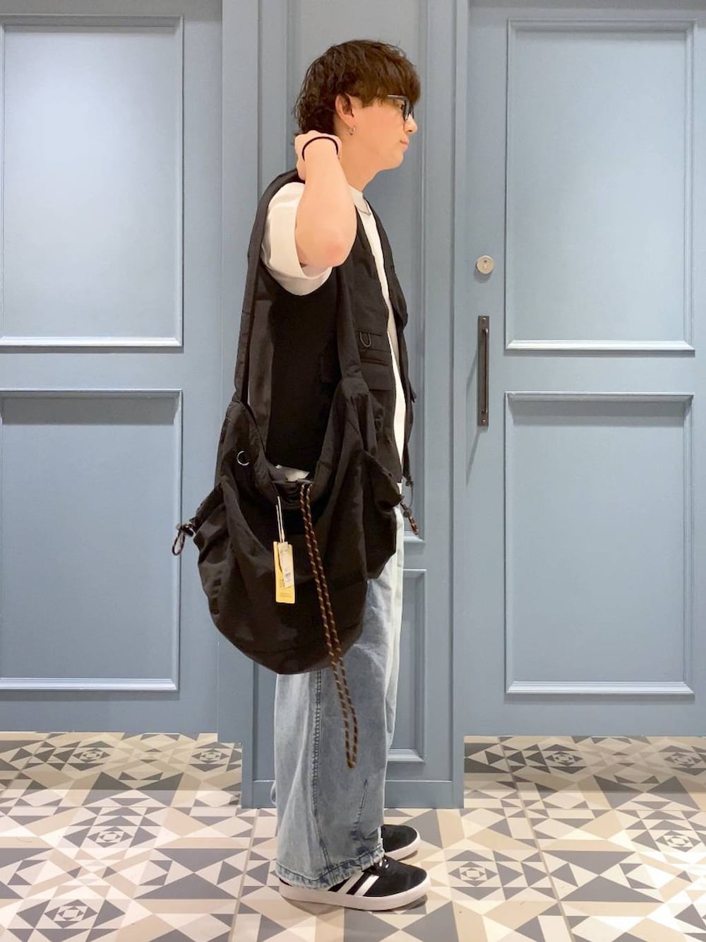 ブルー系のデニムパンツ、ブラック系のショルダーバッグ、ブラック系のベストを着用したメンズの夏コーディネートの2枚目の写真