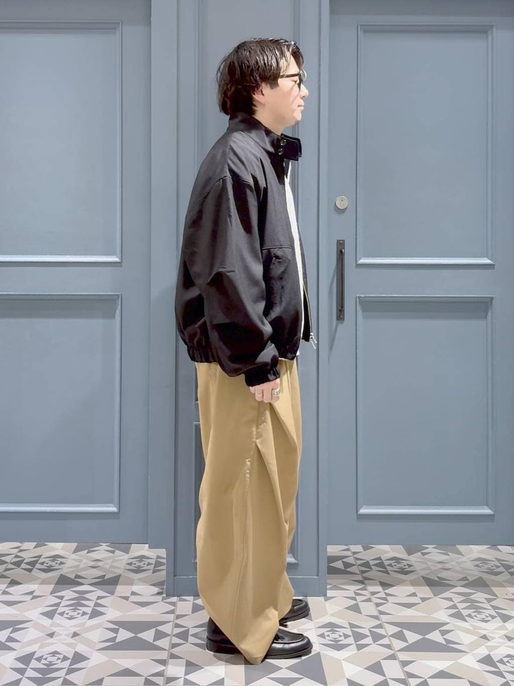 ブラック系のローファー、ブラック系のブルゾン、グレー系のポロシャツを着用したメンズの春コーディネートの2枚目の写真