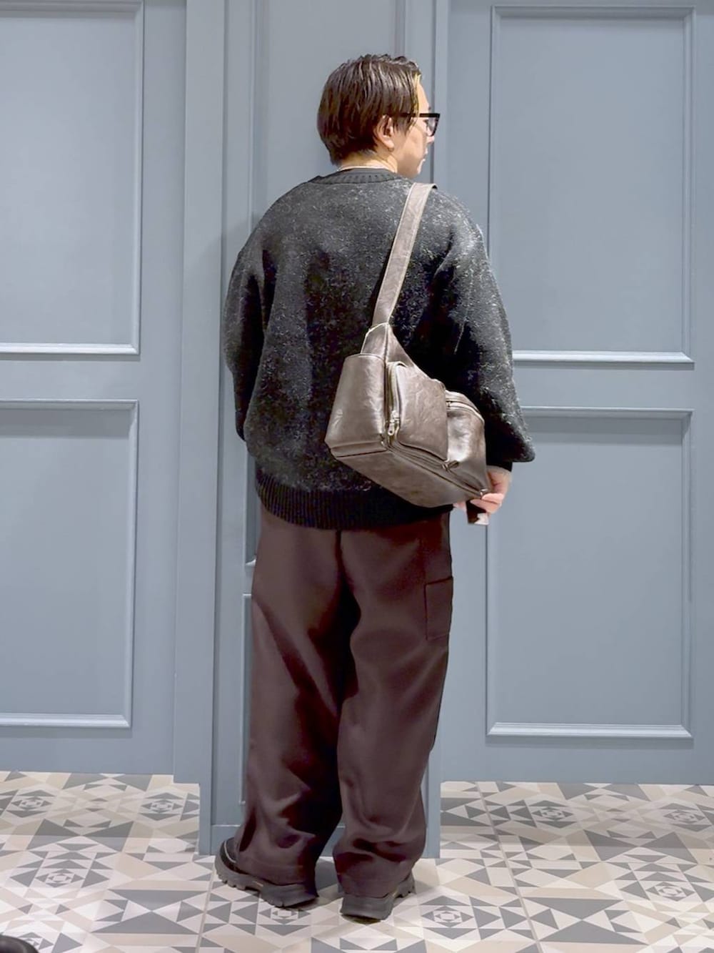 ブラウン系のショルダーバッグ、ブラック系のニット/セーター、ブラウン系のスラックスを着用したメンズの秋コーディネートの3枚目の写真