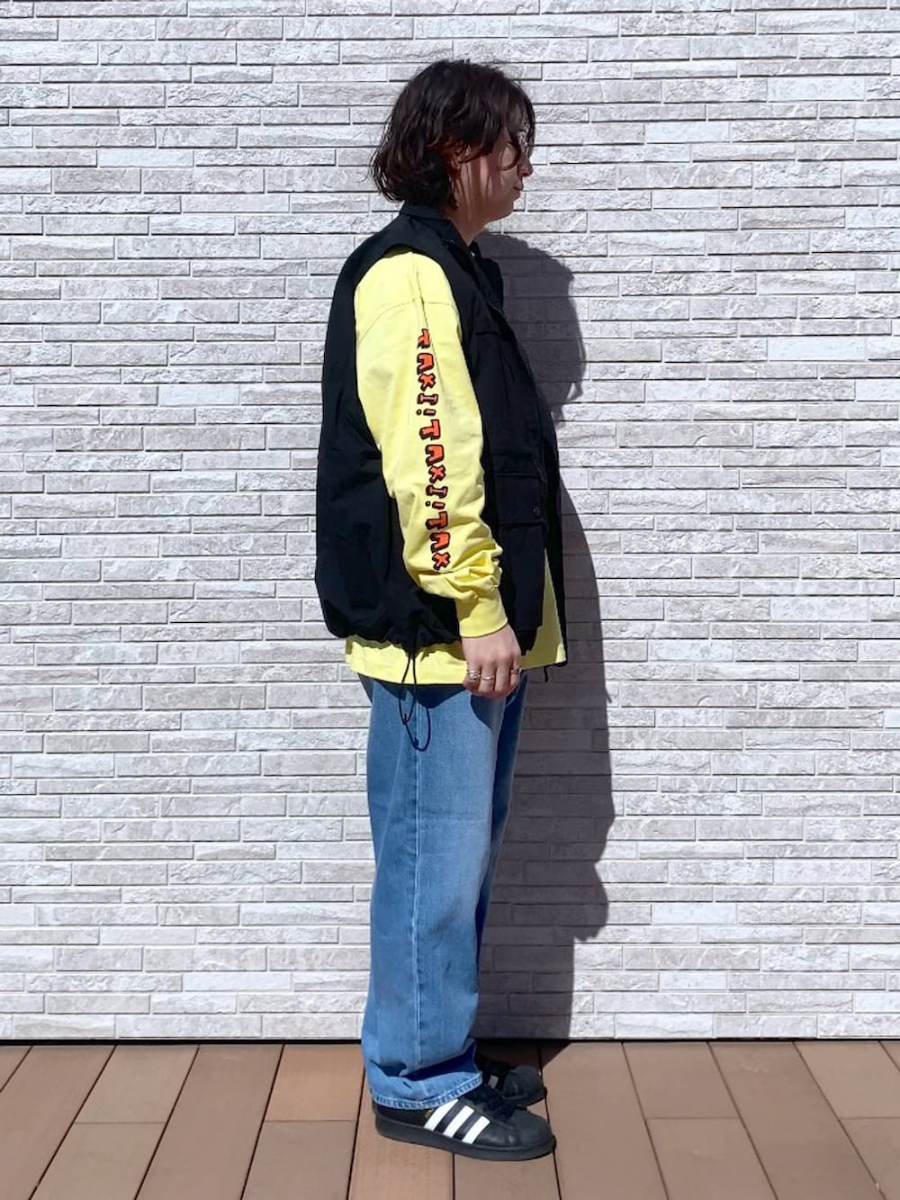 イエロー系のTシャツ/カットソー、ブルー系のデニムパンツ、ブラック系のナイロンジャケットを着用したメンズの春コーディネートの2枚目の写真