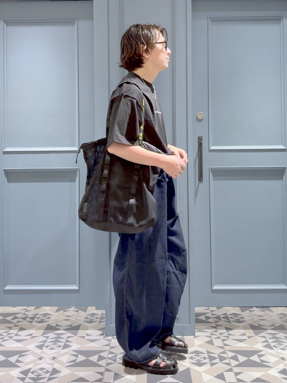 ブラック系のトートバッグ、ブラック系のサンダル、ブルー系のデニムパンツを着用したメンズの夏コーディネートの2枚目の写真