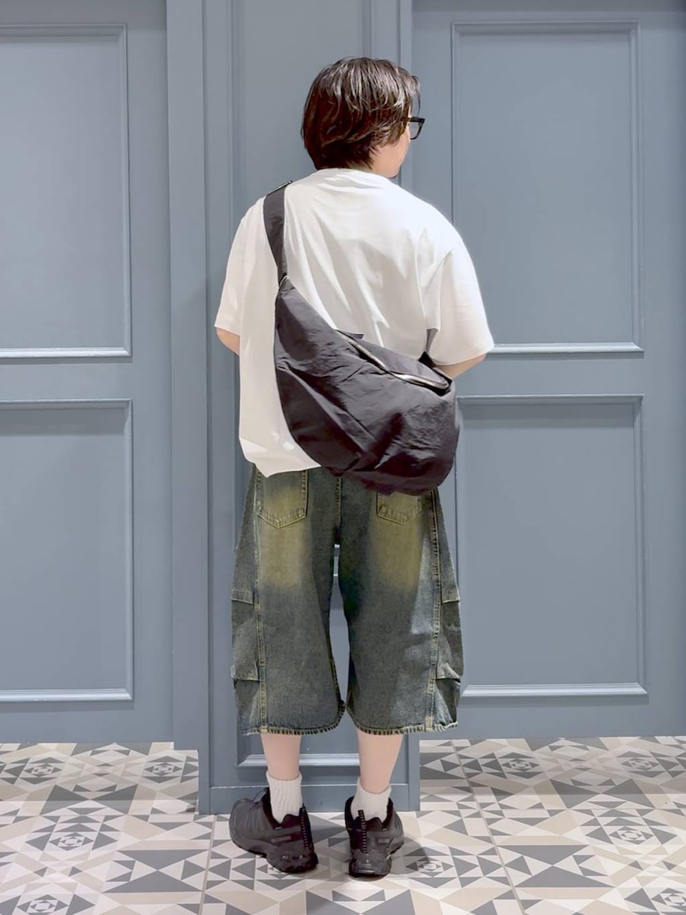 ブルー系のデニムパンツ、ブラック系のスニーカー、ブラック系のショルダーバッグを着用したメンズの夏コーディネートの3枚目の写真