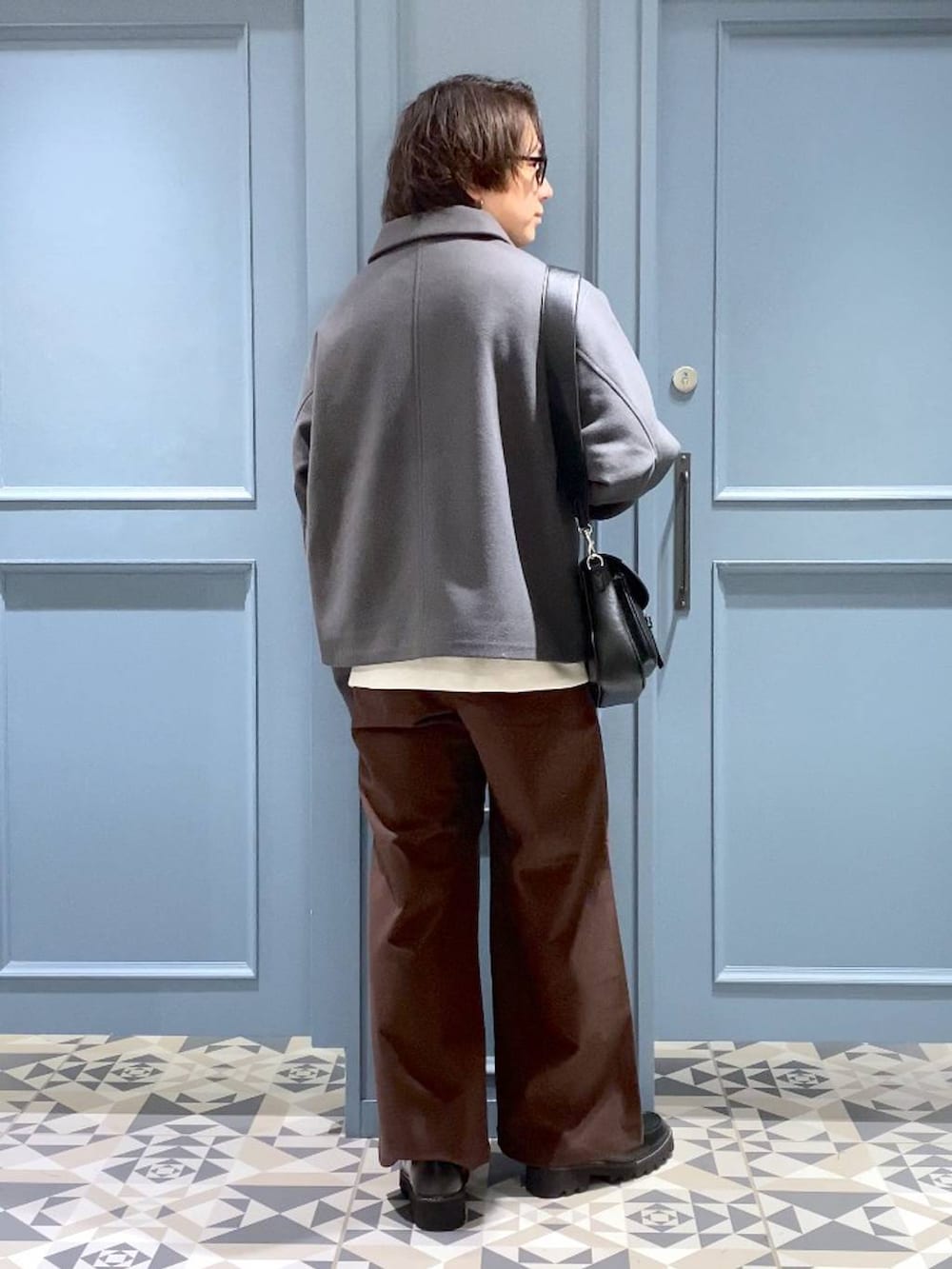 グレー系のブルゾン、ブラウン系のスラックス、ブラック系のショルダーバッグを着用したメンズの冬コーディネートの3枚目の写真