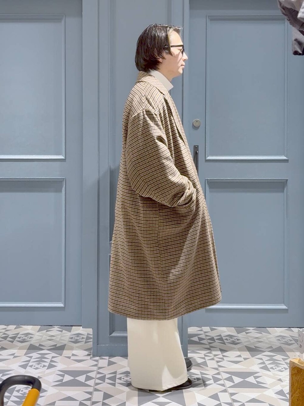 ブラウン系のチェスターコート、レッド系のニット/セーター、ホワイト系のスラックスを着用したメンズの冬コーディネートの2枚目の写真