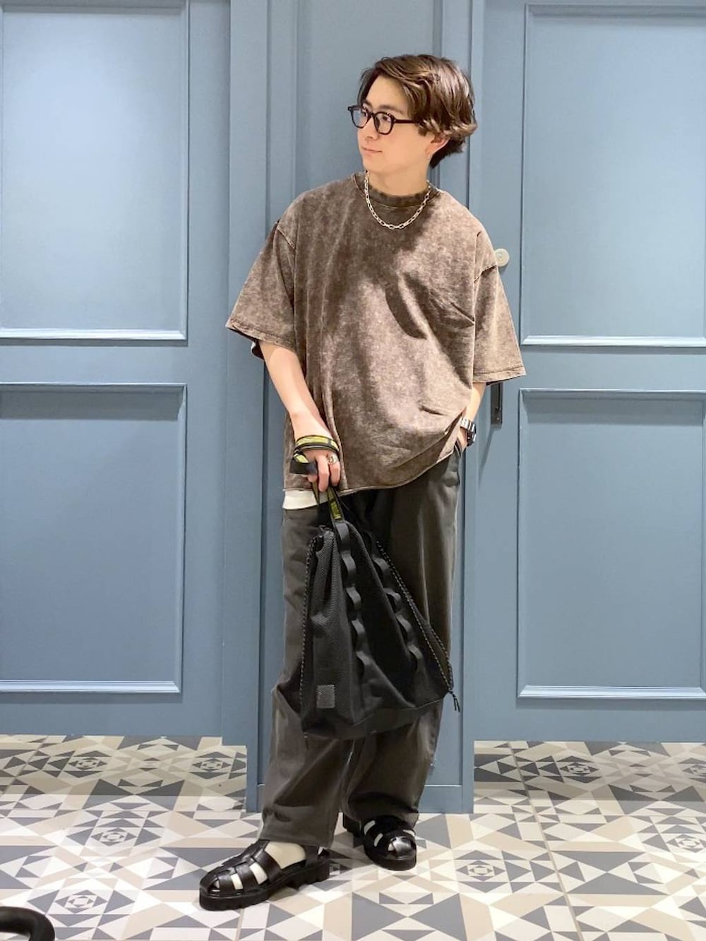 ブラウン系のTシャツ/カットソー、ブラック系のトートバッグ、ブラック系のサンダルを着用したメンズの春コーディネートの4枚目の写真