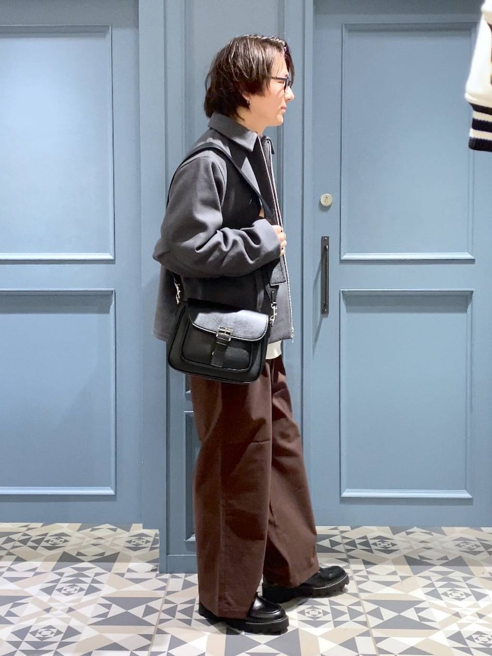 グレー系のブルゾン、ブラウン系のスラックス、ブラック系のショルダーバッグを着用したメンズの冬コーディネートの2枚目の写真