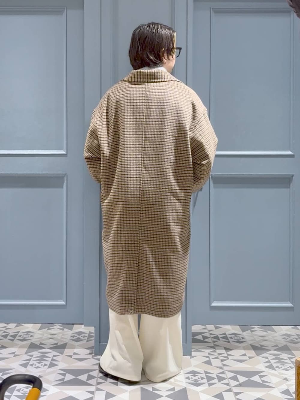 ブラウン系のチェスターコート、グレー系のポロシャツ、ホワイト系のスラックスを着用したメンズの冬コーディネートの3枚目の写真