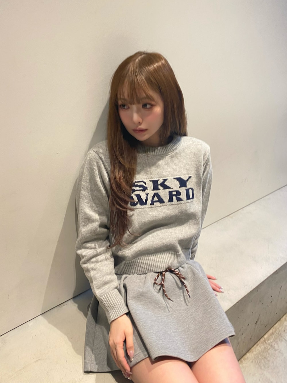 グレー系のニット/セーター、グレー系のスカート、シルバー系のスニーカーを着用したレディースの冬コーディネートの2枚目の写真