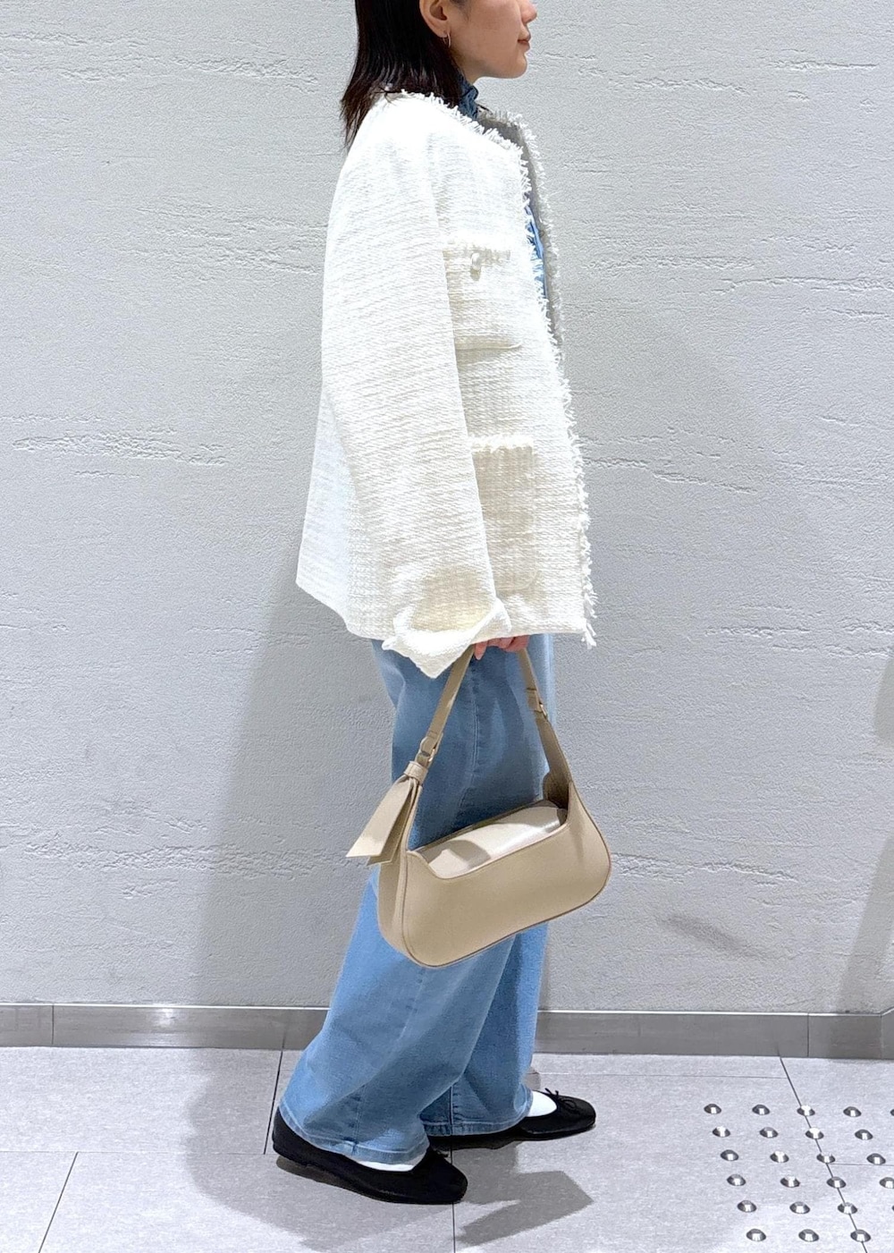 ブルー系のデニムパンツ、ベージュ系のハンドバッグ、ホワイト系のノーカラージャケットを着用したレディースの冬コーディネートの2枚目の写真