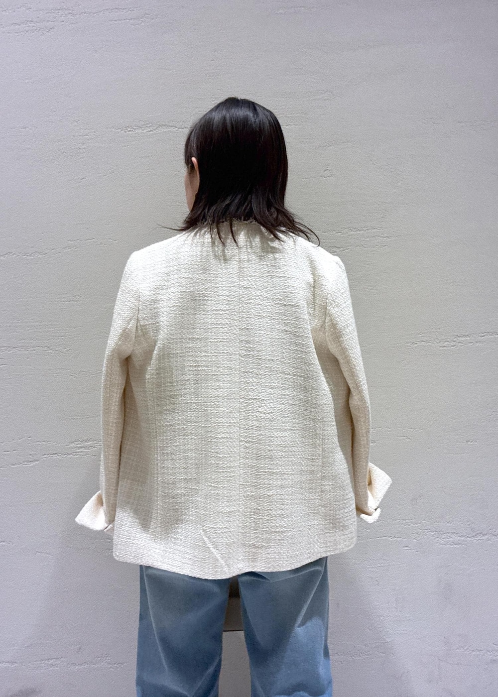 ブルー系のデニムパンツ、ベージュ系のハンドバッグ、ホワイト系のノーカラージャケットを着用したレディースの冬コーディネートの6枚目の写真