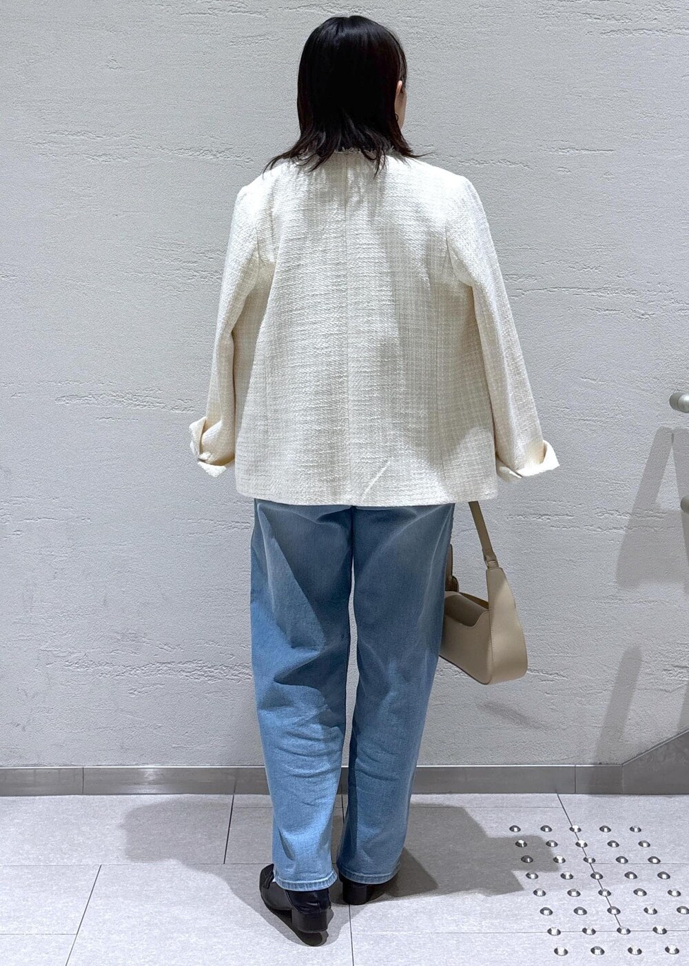 ブルー系のデニムパンツ、ベージュ系のハンドバッグ、ホワイト系のノーカラージャケットを着用したレディースの冬コーディネートの3枚目の写真