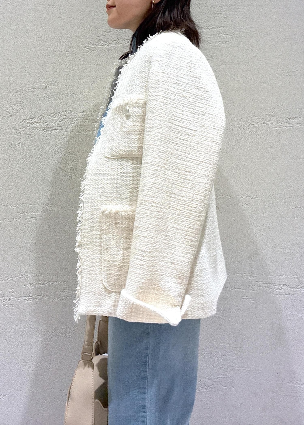 ブルー系のデニムパンツ、ベージュ系のハンドバッグ、ホワイト系のノーカラージャケットを着用したレディースの冬コーディネートの5枚目の写真