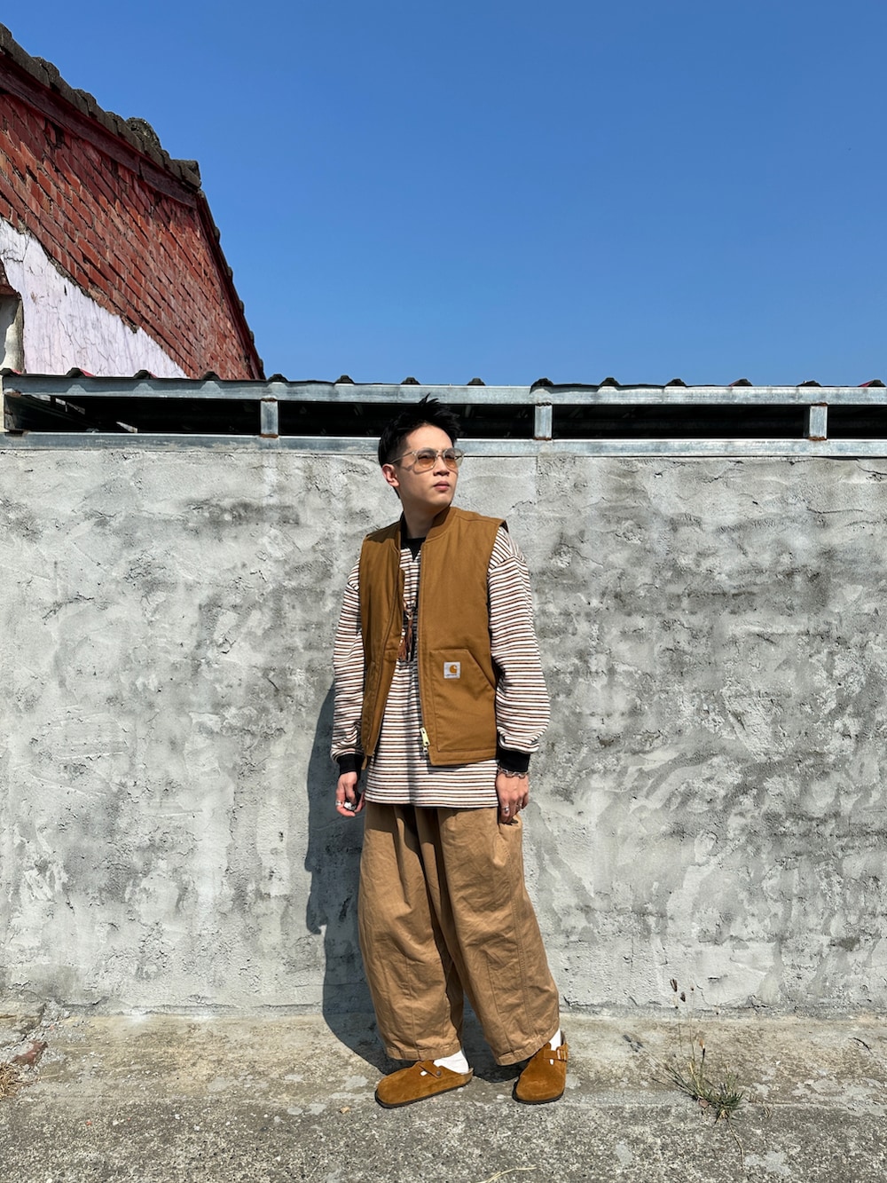 イエロー系のポロシャツ、ブラウン系のベスト、ブラウン系のサンダルを着用したメンズの春コーディネートの2枚目の写真