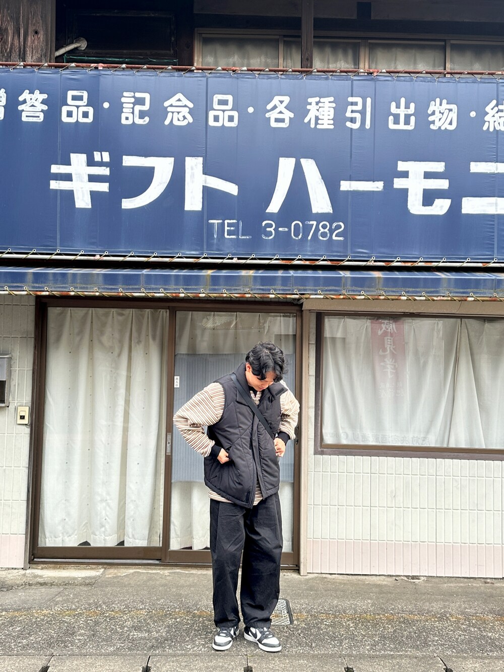 イエロー系のポロシャツ、ブラック系のベスト、ブラック系のスニーカーを着用したメンズの冬コーディネートの2枚目の写真