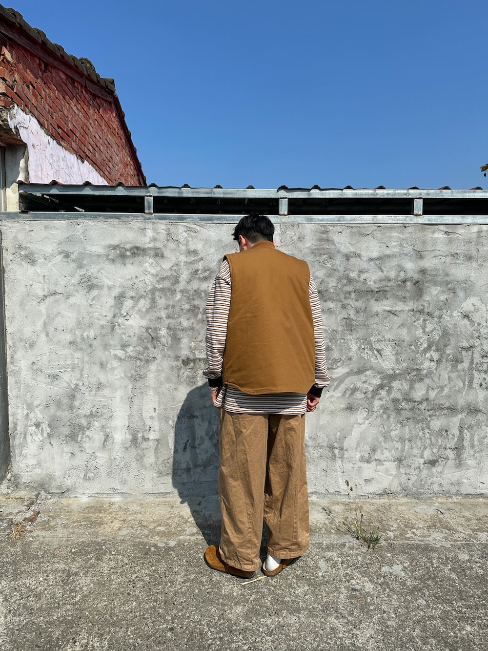 イエロー系のポロシャツ、ブラウン系のベスト、ブラウン系のサンダルを着用したメンズの春コーディネートの3枚目の写真