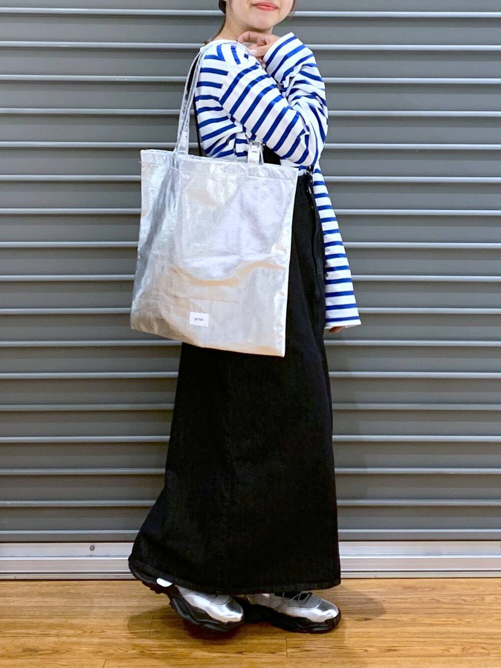 シルバー系のトートバッグ、グレー系のスニーカー、ブラック系のジャンパースカートを着用したレディースの春コーディネートの5枚目の写真