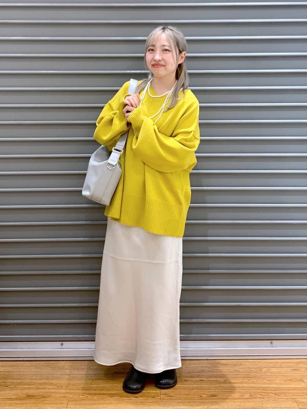 イエロー系のニット/セーター、ホワイト系のスカート、グレー系のショルダーバッグを着用したレディースの冬コーディネートの4枚目の写真