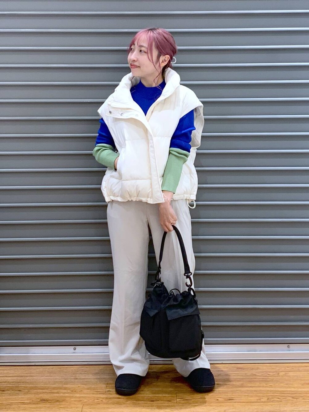 ブラック系のショルダーバッグ、ブルー系のニット/セーター、ホワイト系のダウンベストを着用したレディースの秋コーディネートの3枚目の写真