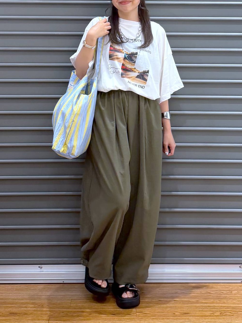 ブルー系のトートバッグ、ホワイト系のTシャツ/カットソー、ブラック系のサンダルを着用したレディースの夏コーディネートの6枚目の写真