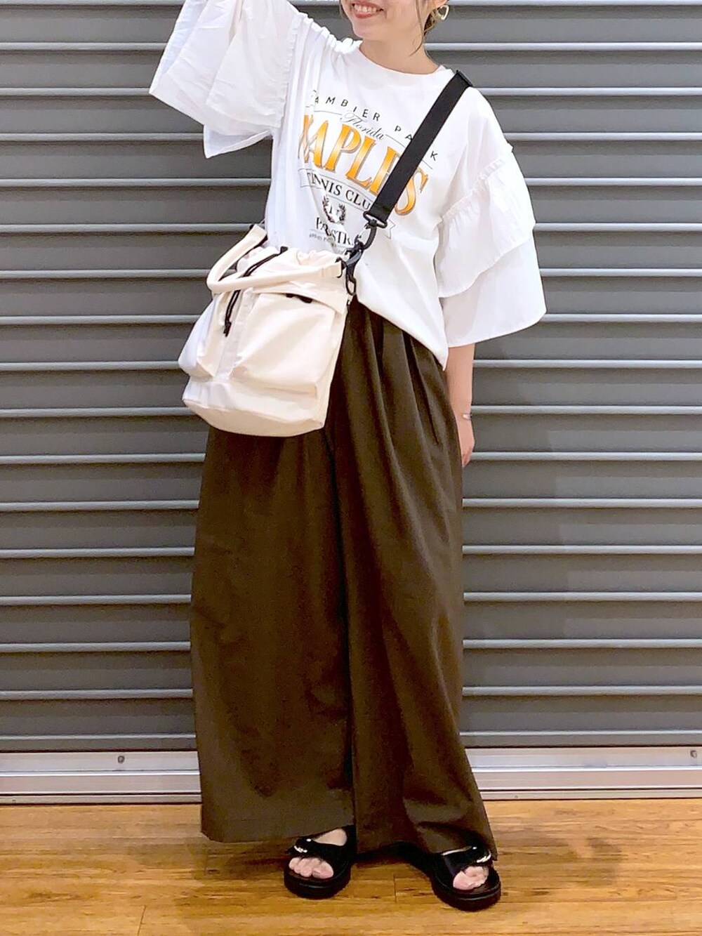 ホワイト系のショルダーバッグ、ブラック系のサンダル、ブラウン系のスラックスを着用したレディースの夏コーディネートの4枚目の写真