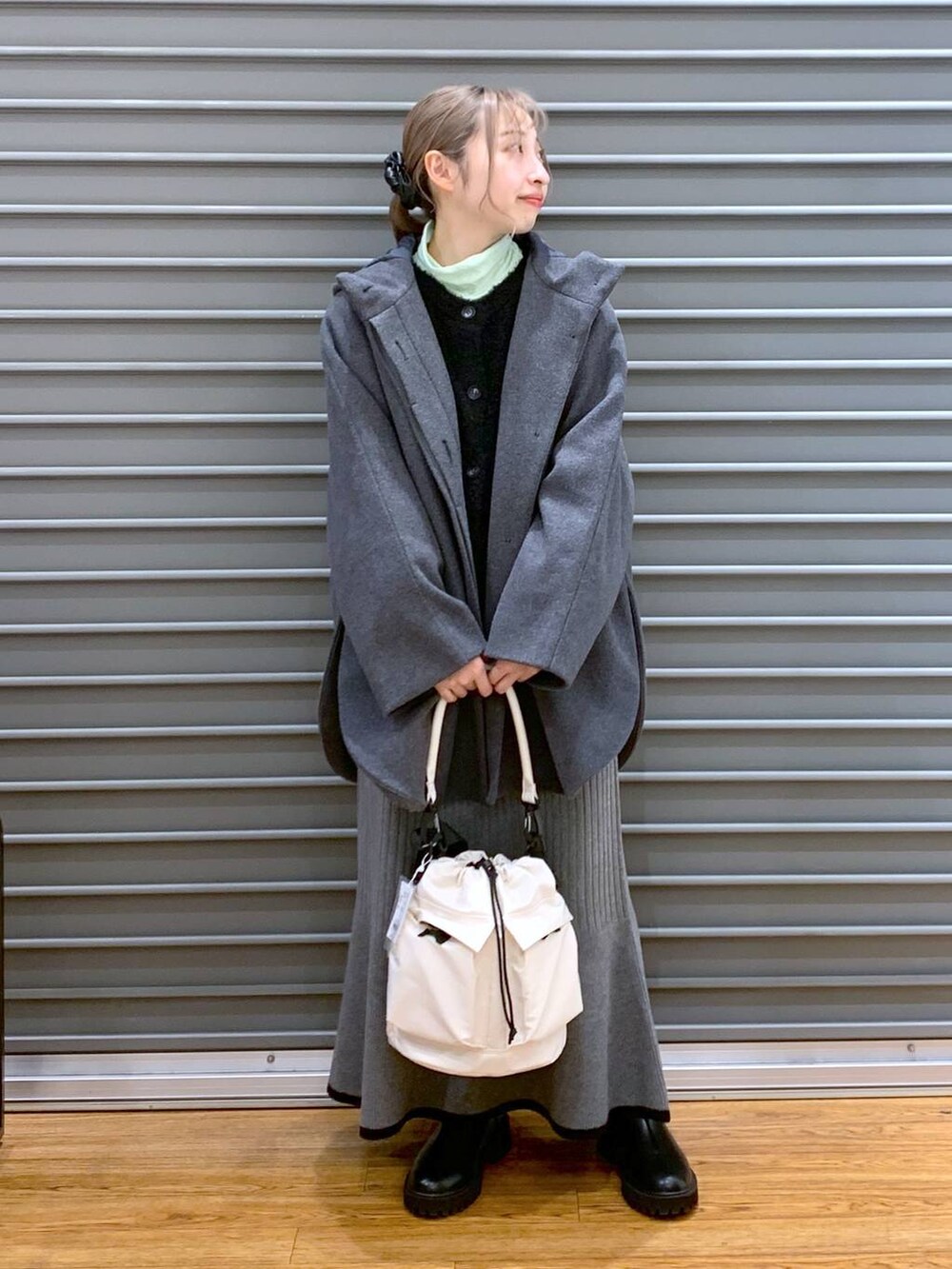 ホワイト系のショルダーバッグ、グレー系のポンチョ、ブラック系のブーツを着用したレディースの冬コーディネートの3枚目の写真