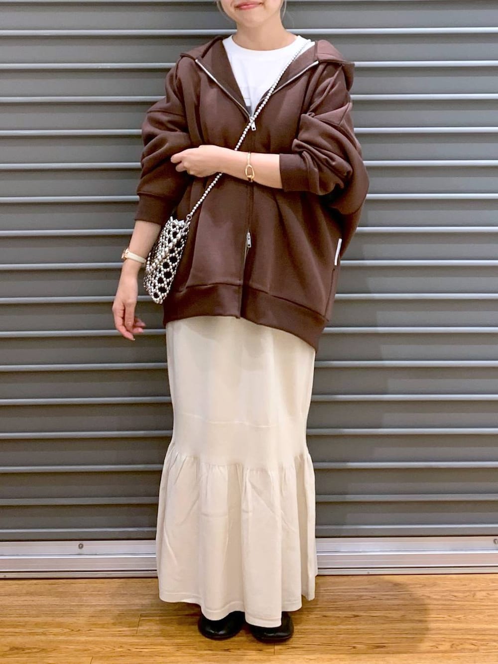 シルバー系のショルダーバッグ、ホワイト系のスカート、ブラウン系のパーカーを着用したレディースの秋コーディネートの5枚目の写真