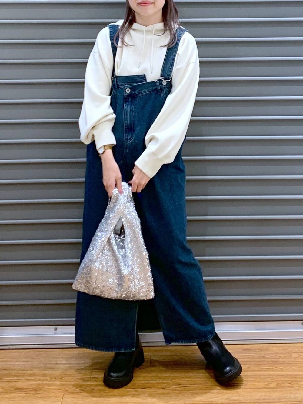 ブラック系のブーツ、ブルー系のジャンパースカート、ホワイト系のニット/セーターを着用したレディースの秋コーディネートの3枚目の写真