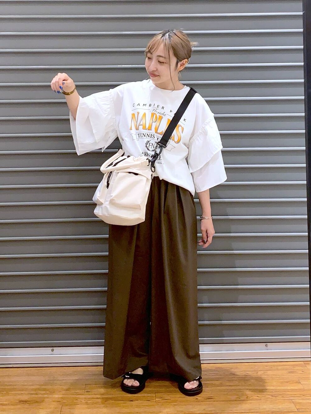 ホワイト系のショルダーバッグ、ブラック系のサンダル、ブラウン系のスラックスを着用したレディースの夏コーディネートの6枚目の写真