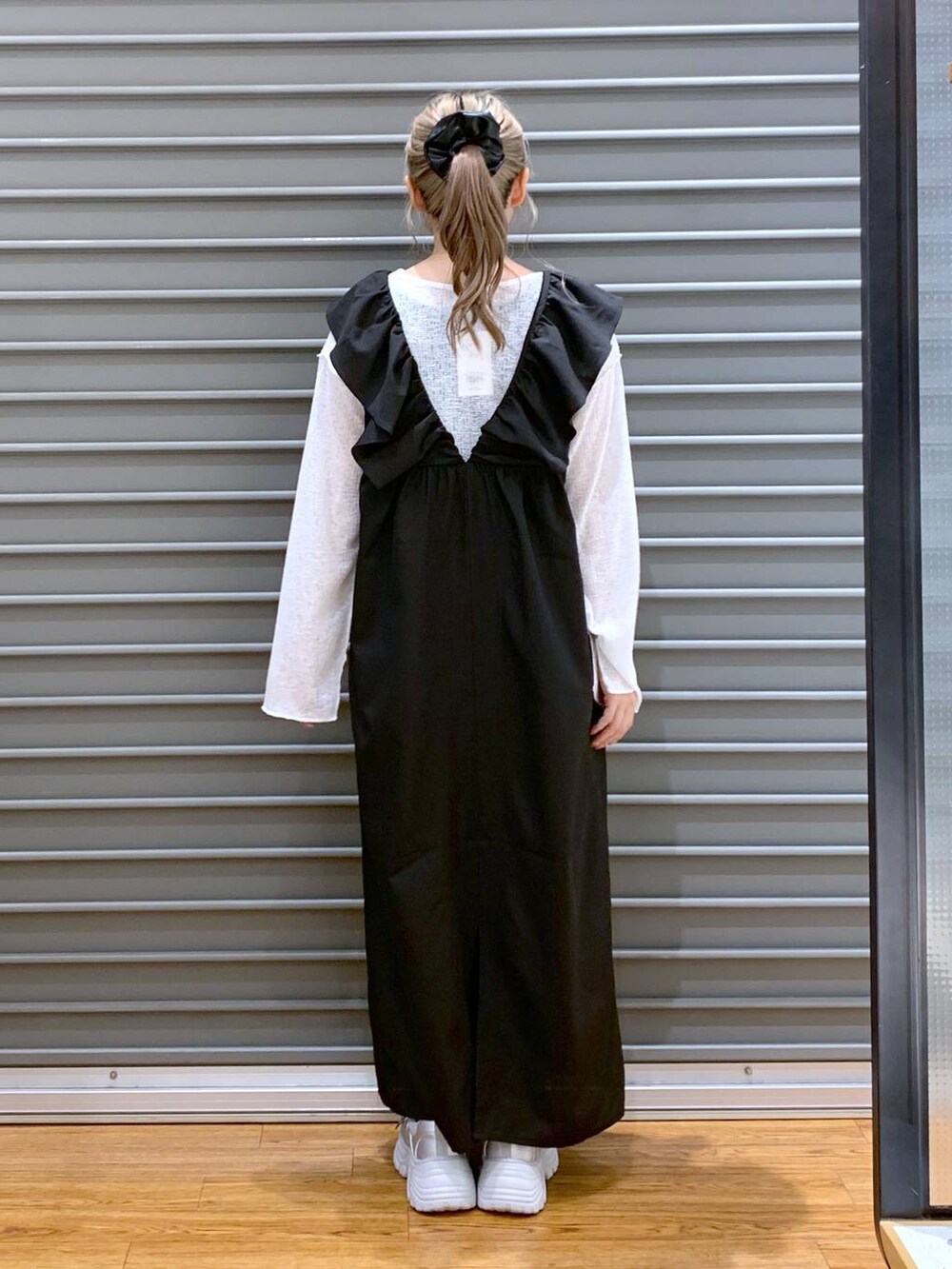 ブラック系のジャンパースカート、シルバー系のスニーカー、ホワイト系のTシャツ/カットソーを着用したレディースの春コーディネートの2枚目の写真