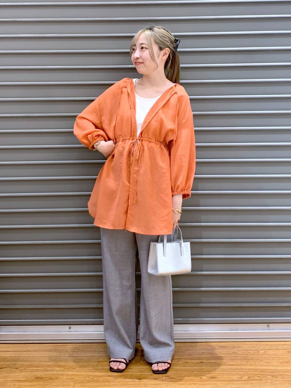 オレンジ系のシャツ/ブラウス、グレー系のショルダーバッグ、ブラック系のサンダルを着用したレディースの夏コーディネートの4枚目の写真