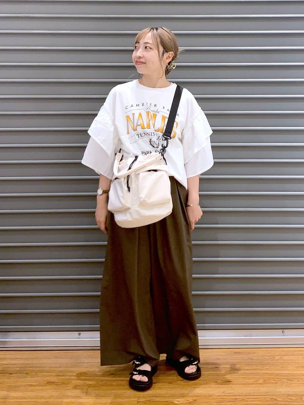 ホワイト系のショルダーバッグ、ブラック系のサンダル、ブラウン系のスラックスを着用したレディースの夏コーディネートの3枚目の写真