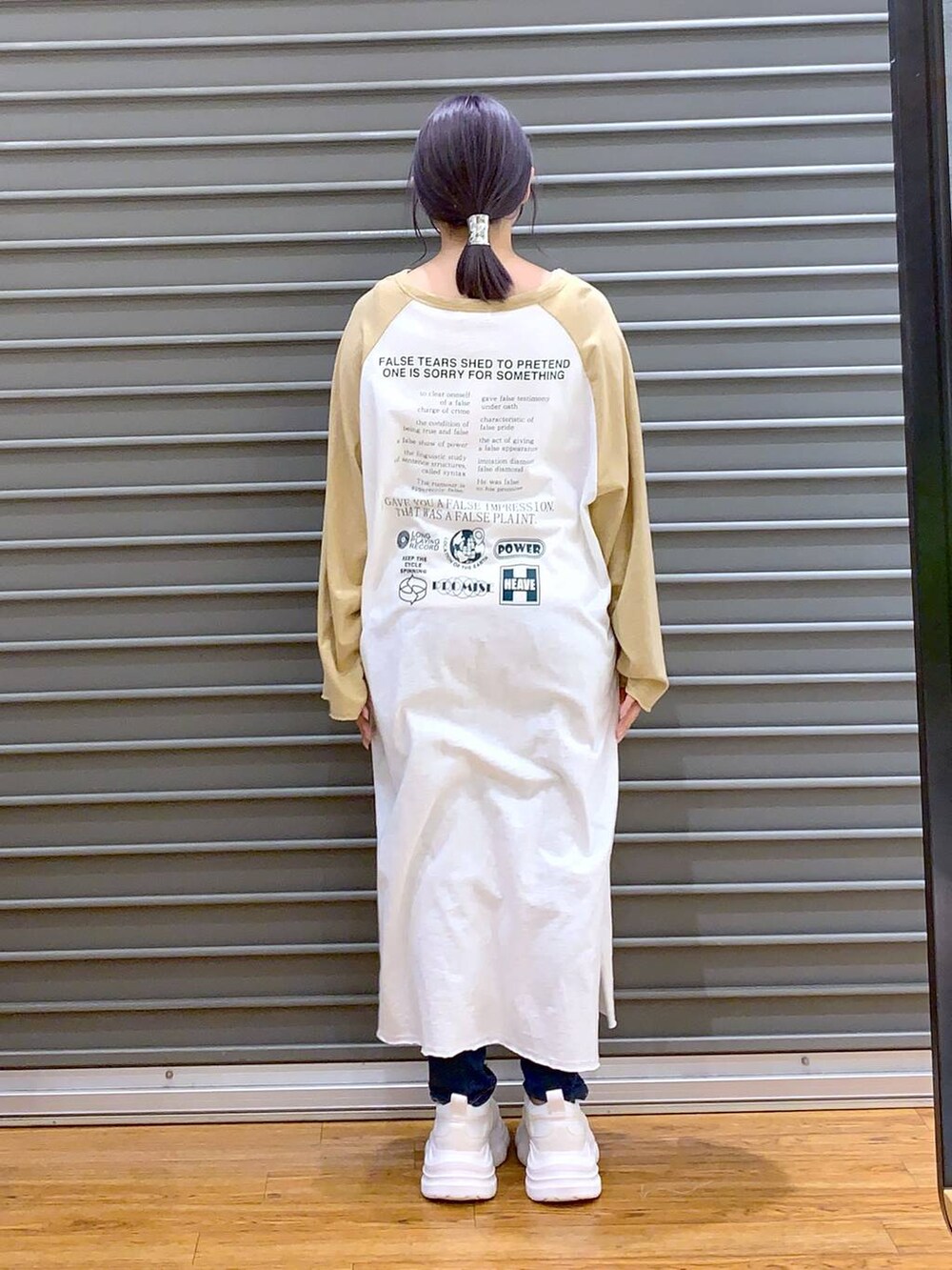 ベージュ系のワンピース、ホワイト系のスニーカー、ブルー系のデニムパンツを着用したレディースの春コーディネートの2枚目の写真