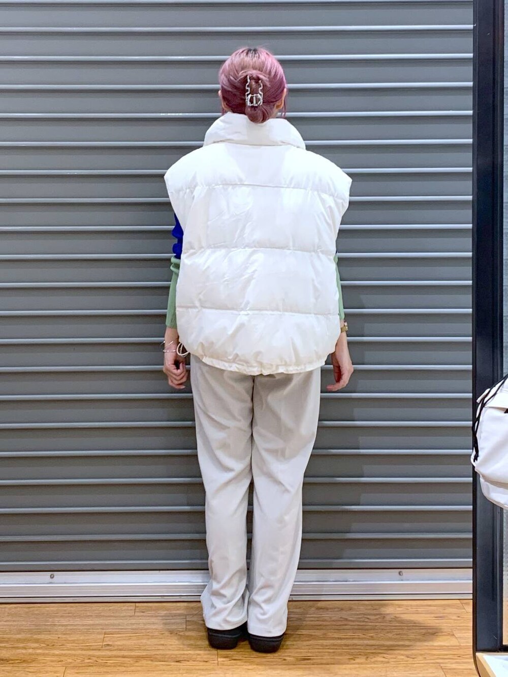 ブラック系のショルダーバッグ、ブルー系のニット/セーター、ホワイト系のダウンベストを着用したレディースの秋コーディネートの2枚目の写真