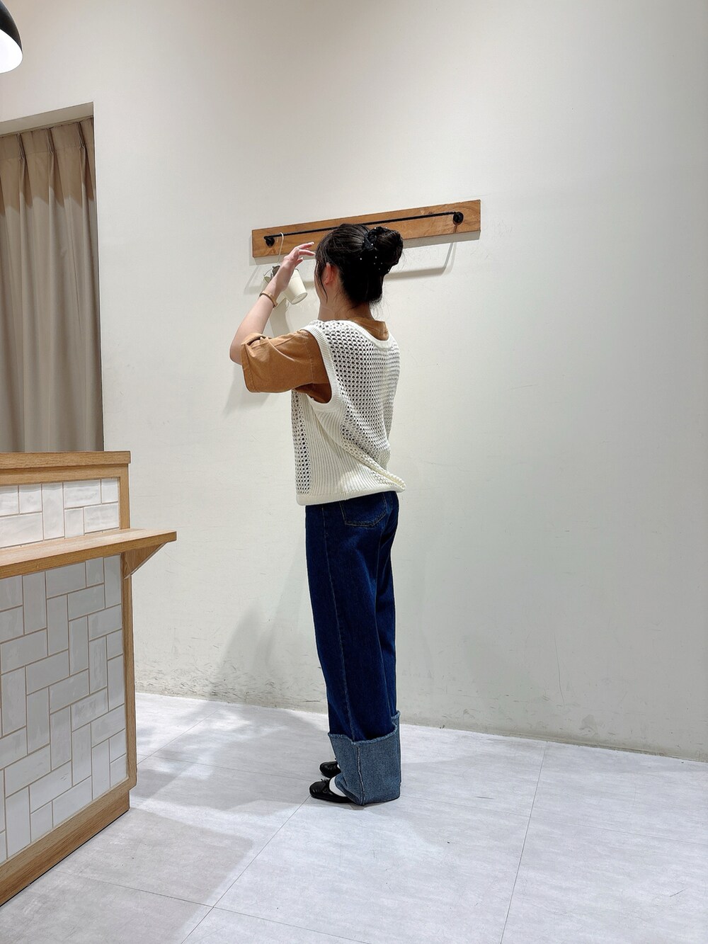 ホワイト系のベスト、ブラウン系のトップス、ブルー系のデニムパンツを着用したレディースの春コーディネートの2枚目の写真