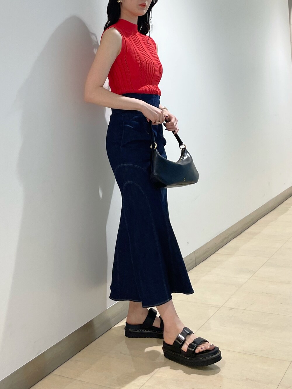 ブラック系のハンドバッグ、レッド系のニット/セーター、ブルー系のデニムスカートを着用したレディースの夏コーディネートの2枚目の写真
