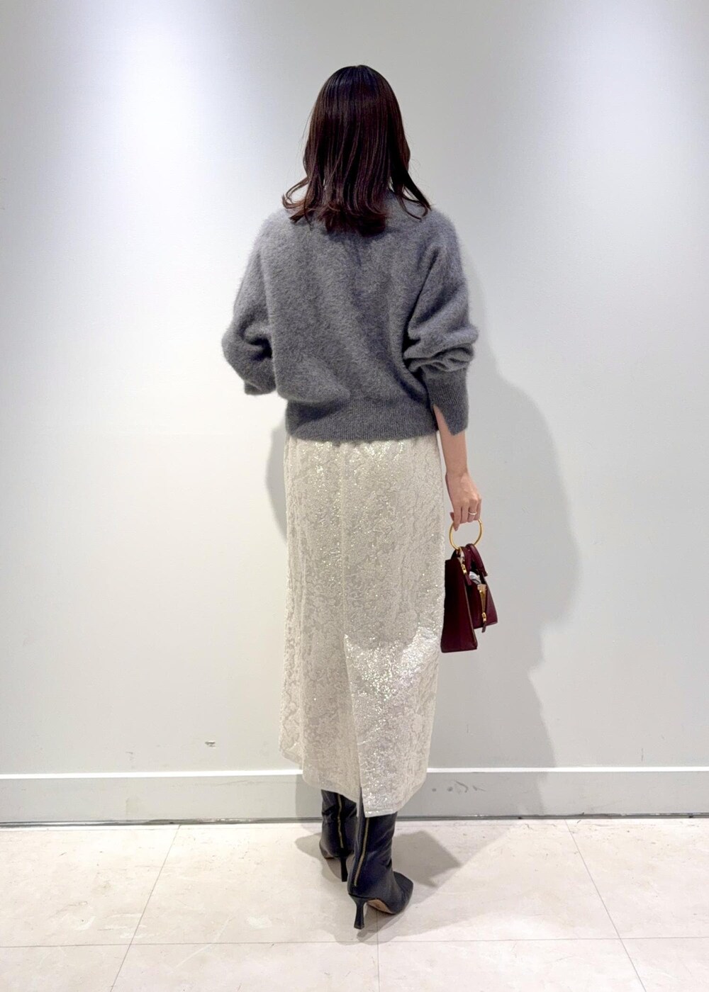 レッド系のショルダーバッグ、ブラック系のブーツ、グレー系のニット/セーターを着用したレディースの冬コーディネートの2枚目の写真